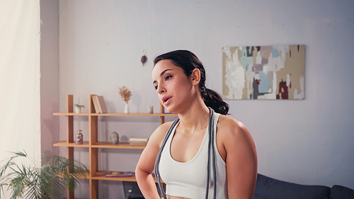 Exhausted sportswoman with jump rope standing in living room