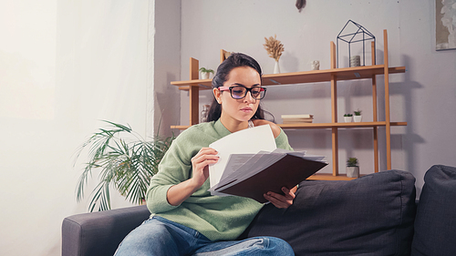 Brunette student in eyeglasses holding papers on couch