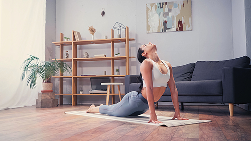 Young pretty sportswoman stretching on fitness mat at home