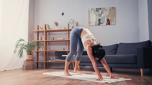 Sportswoman stretching while standing on fitness mat at home