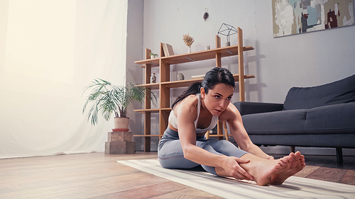 Sportswoman looking away while stretching at home