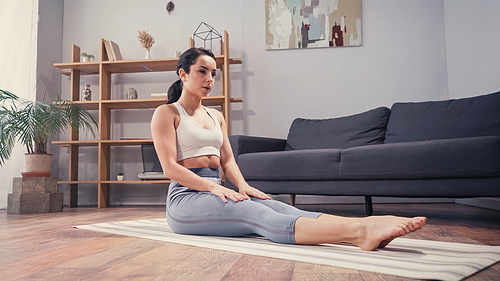 Barefoot sportswoman resting on fitness mat in living room