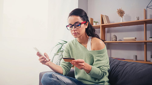 Pretty woman in eyeglasses using credit card and smartphone