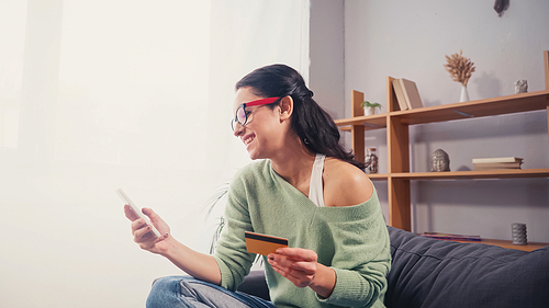 positive woman using credit card and smartphone at home