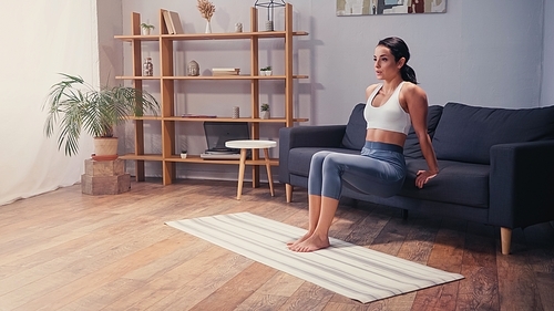 Fit sportswoman working out near couch in living room