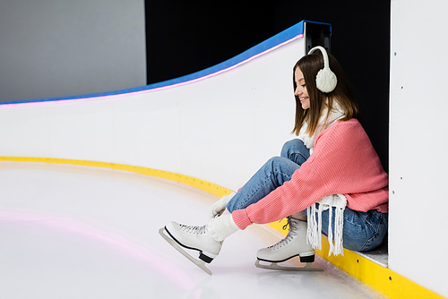 cheerful young woman in winter outfit tying shoe laces on ice skates