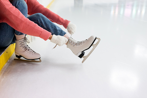 partial view of young woman tying shoe laces on ice skates