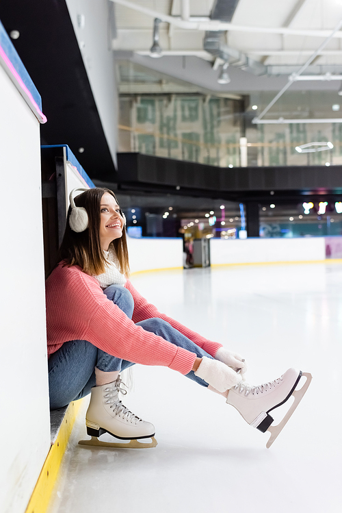 cheerful young woman tying shoe laces on ice skates