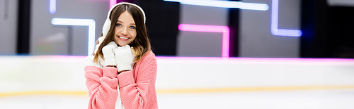 joyful young woman in ear muffs and scarf on ice rink, banner