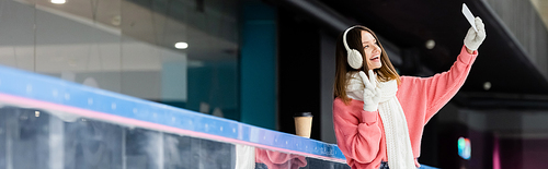 happy woman in ear muffs showing peace sign and taking selfie, banner