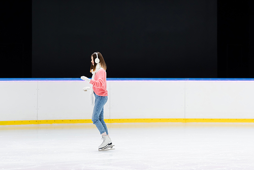 side view of young woman in white ear muffs skating on ice rink