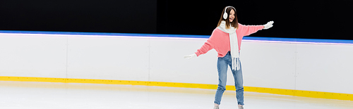 cheerful young woman in ear muffs and scarf skating on ice rink, banner