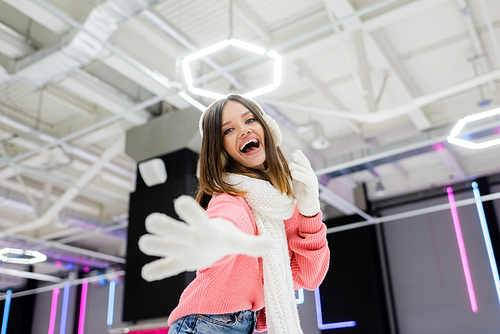 low angle view of excited woman in ear muffs and winter outfit with open mouth