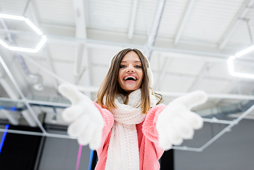 low angle view of cheerful young woman in ear muffs and scarf gesturing while 