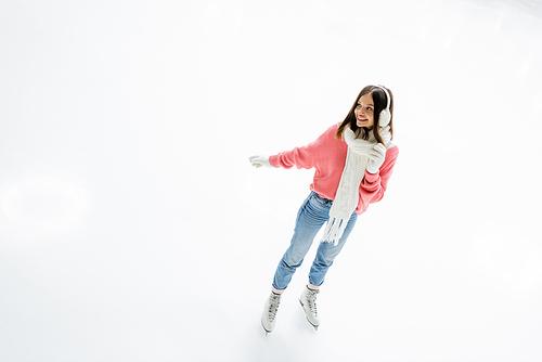 high angle view of positive young woman in ear muffs and scarf skating on ice rink