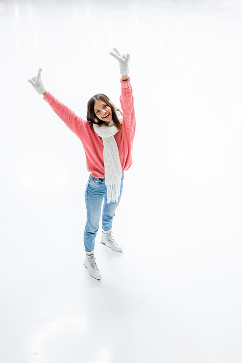 high angle view of cheerful young woman in ear muffs and scarf showing peace sign while skating on ice rink