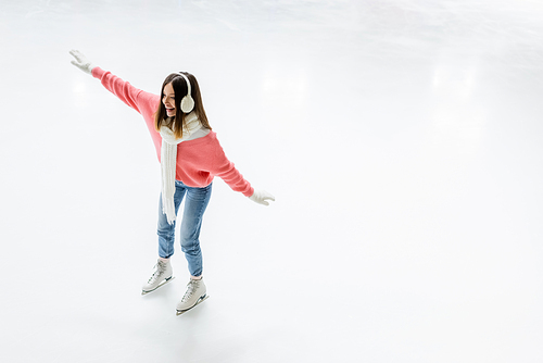high angle view of happy young woman in ear muffs and scarf skating on ice rink