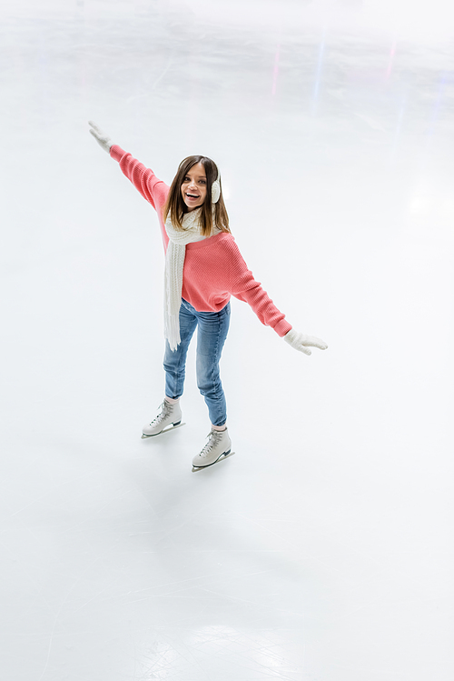 high angle view of amazed young woman in ear muffs and scarf skating on ice rink