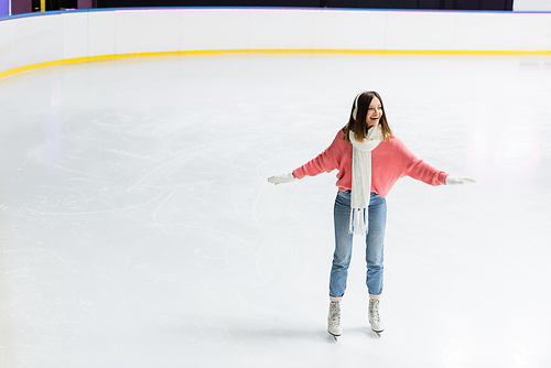 full length of amazed young woman skating with outstretched hands on ice rink