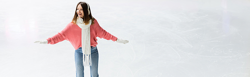 smiling young woman in ear muffs and scarf on ice rink, banner