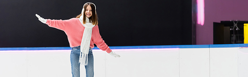 positive young woman in ear muffs and scarf on ice rink, banner