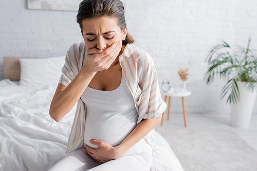young pregnant woman feeling nausea and covering mouth in bedroom