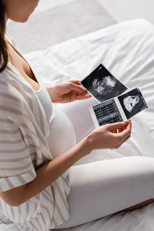 partial view of pregnant woman holding ultrasound scans