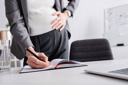 cropped view of pregnant businesswoman writing in notebook