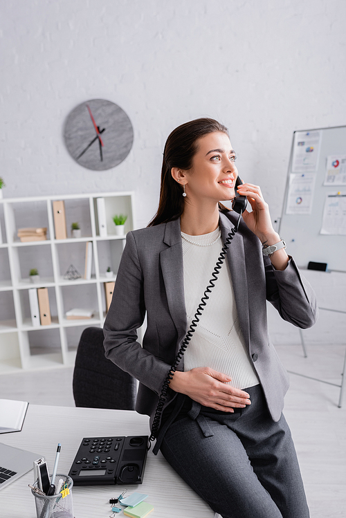 happy pregnant businesswoman talking on retro telephone in office