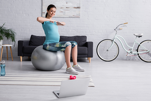 smiling pregnant woman exercising on fitness ball in modern living room
