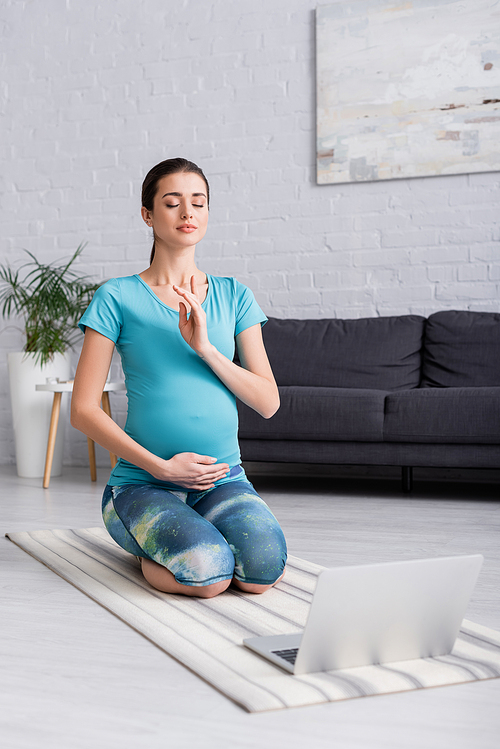 young pregnant woman with closed eyes meditating in living room