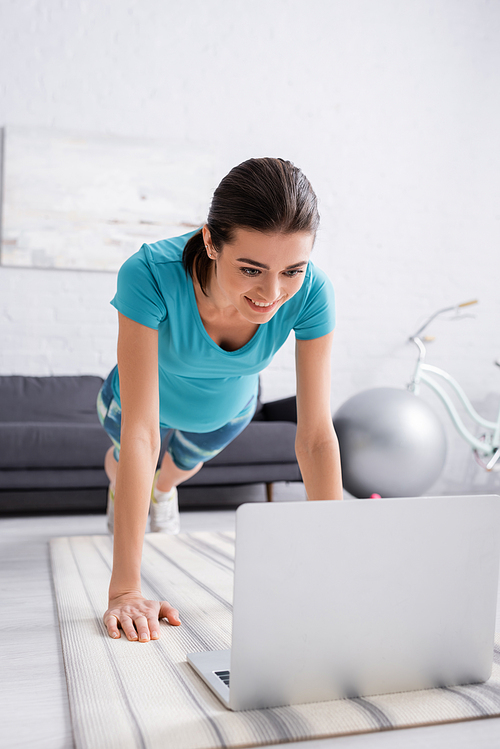joyful pregnant woman in sportswear exercising near laptop in living room