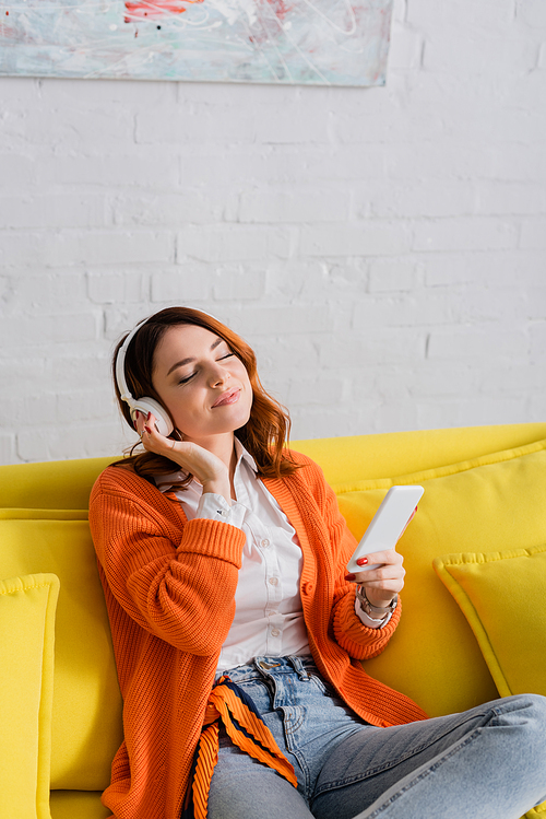 smiling woman in headphones holding smartphone while listening music with closed eyes