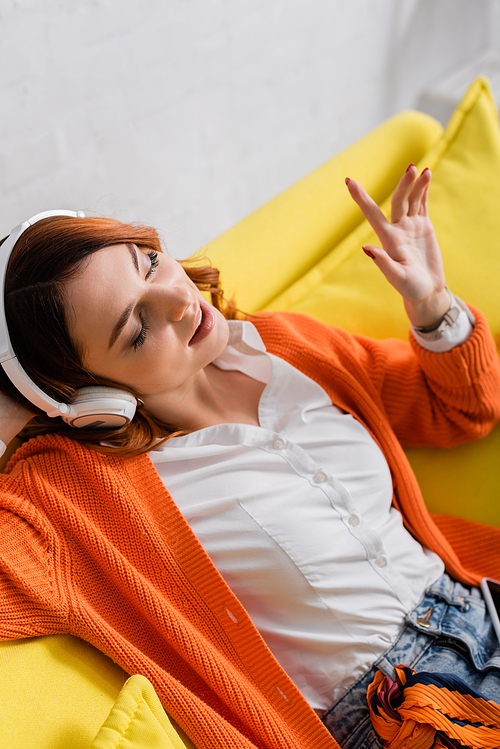 joyful woman with closed eyes gesturing while listening music in headphones