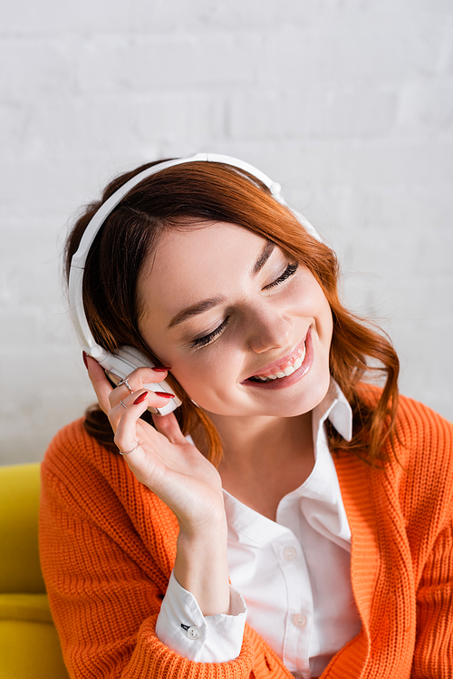 young woman with closed eyes smiling while listening music in wireless headphones