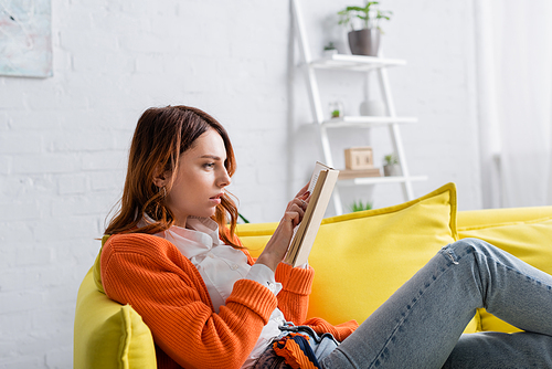 tense woman reading book while sitting on yellow sofa