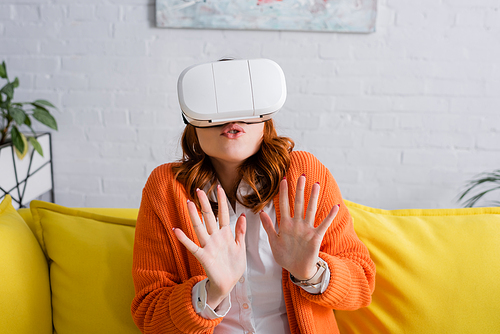 scared woman in vr headset showing stop gesture while gaming at home