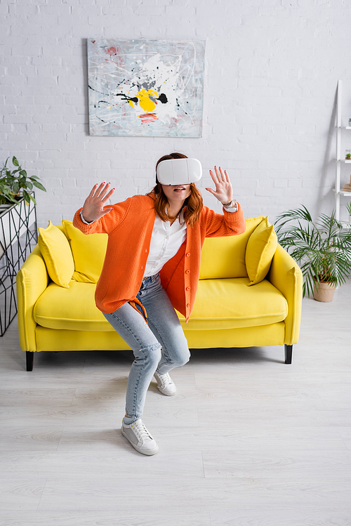 full length view of young woman gaming in vr headset near yellow sofa in living room
