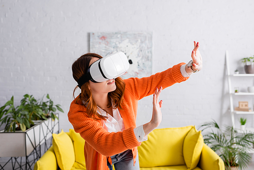 young woman in vr headset gesturing with outstretched hands while gaming in living room