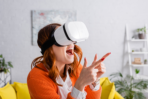 excited woman in vr headset pointing with fingers while gaming at home