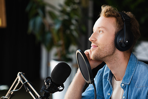 positive radio host in headphones looking away in podcast studio