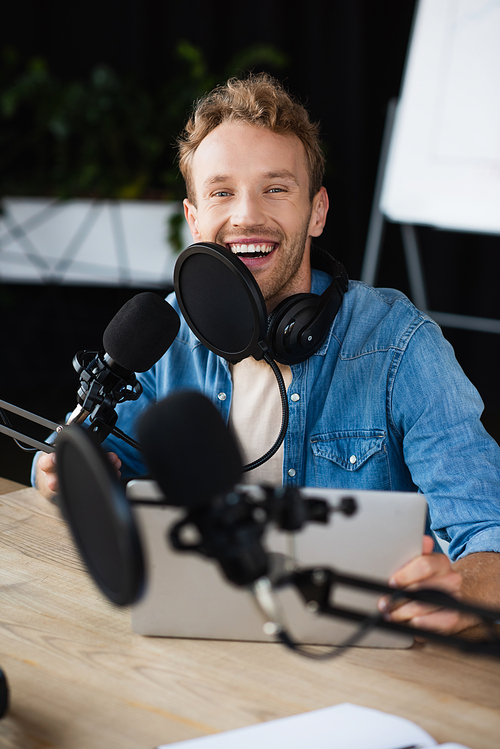 positive radio host in headphones smiling in podcast studio