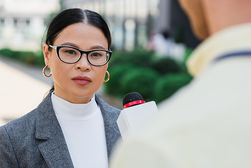 asian businesswoman in glasses  near blurred journalist
