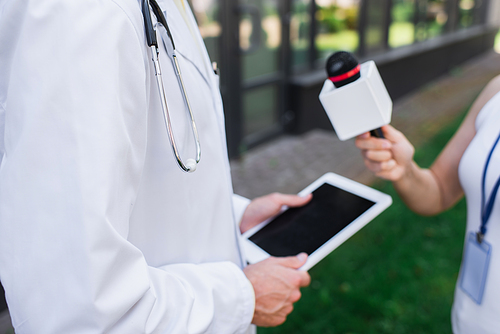 cropped view of doctor in white coat holding digital tablet while giving interview to journalist with microphone