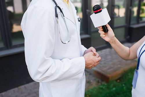 cropped view of doctor in white coat giving interview to journalist with microphone