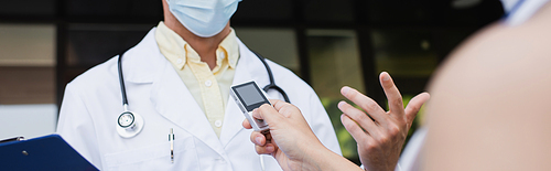 cropped view of blurred reporter holding voice recorder near doctor in medical mask gesturing during interview, banner