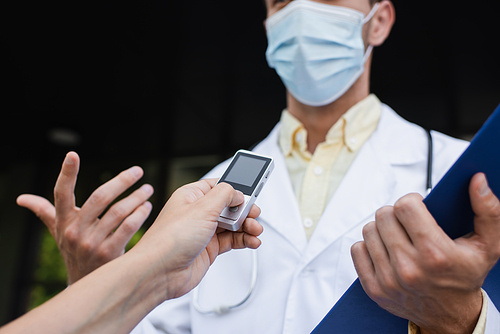 cropped view of reporter holding voice recorder near doctor in medical mask gesturing during interview