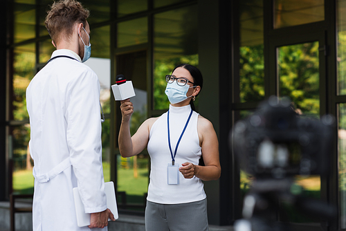 asian reporter in medical mask holding microphone near doctor in white coat
