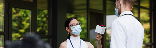 asian reporter in medical mask holding microphone near doctor in white coat, banner
