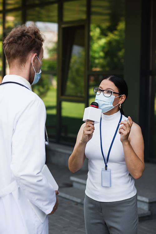 asian reporter in medical mask talking in microphone near doctor in white coat with digital tablet